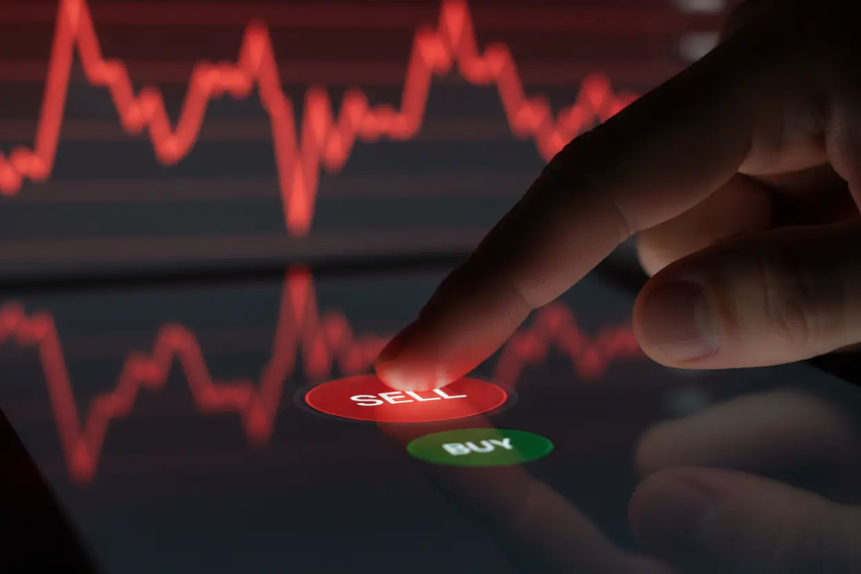 Mão sobre botão de venda em plataforma de Day Trade com gráfico volátil