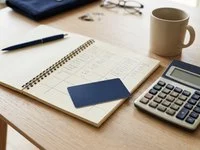 Cartão de plástico liso ao lado de uma calculadora e de um caderno sobre uma mesa de madeira clara