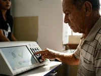 Eleitor idoso votando na urna eletrônica durante o segundo turno para confirmação da prova de vida do INSS.