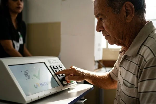 Eleitor idoso votando na urna eletrônica durante o segundo turno para confirmação da prova de vida do INSS.